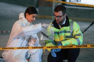 Holding ,knife in package. Two detectives are collecting evidence in a crime scene photo