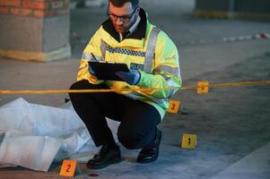 Male ,detective is collecting evidence in a crime scene near dead body on the construction site. Sitting with notepad in hands photo