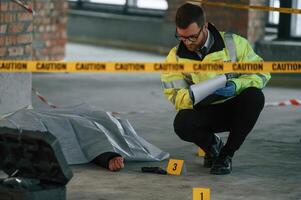 Notepad with information. Male detective is collecting evidence in a crime scene near dead body on the construction site photo