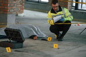 Notepad ,with, information.. Male detective is collecting evidence in a crime scene near dead body on the construction site photo