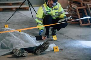 Knife ,is on the floor.. Male detective is collecting evidence in a crime scene near dead body on the construction site photo