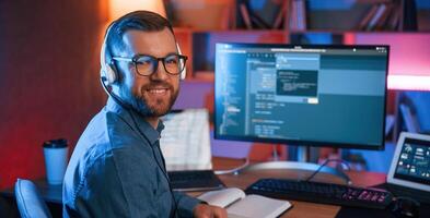 Sitting and ,,smiling. Professiona,l programmer is working indoors. Neon lighting photo