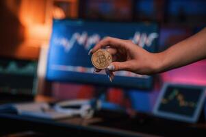 Close up view of woman's ,hand that holding bitcoin against computer display and tablet with graphs photo