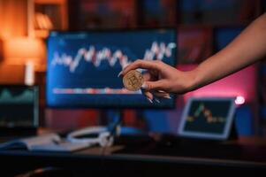 Close up view of woman's hand, that holding bitcoin against computer display and tablet with graphs photo