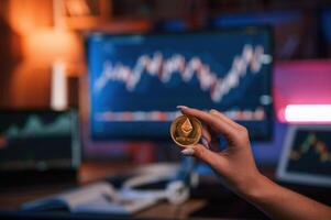 Close up, view of woman's hand that holding bitcoin against computer display and tablet with graphs photo