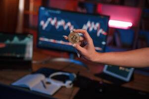 Close up view ,of woman's hand that holding bitcoin against computer display and tablet with graphs photo