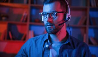 Portrait of man that, is sitting by a computer indoors at home. Neon lighting photo