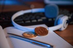 Close up, view of physical bitcoins, headphones, notepad and pen that is on the table photo