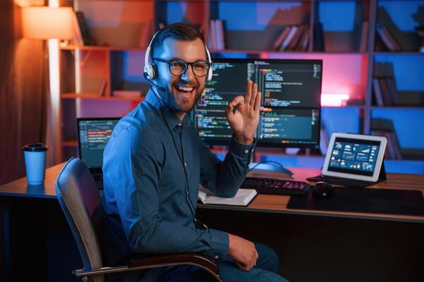 Positive professiona,l programmer is working indoors and smiling. Neon lighting