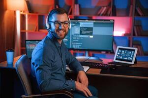 Positive, professional ,programmer is working indoors and smiling. Neon lighting photo