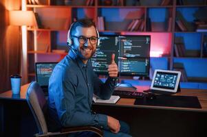 Showing thumb up. Professiona,l programmer i,s working indoors. Neon lighting photo