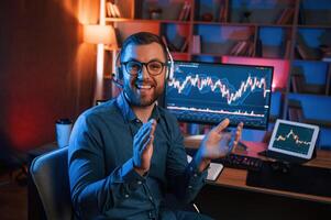 Sitting and ,looking at the camera. Stock, trader is working by pc indoors. Conception of exchange and money photo