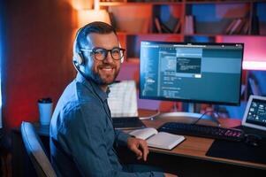Sitting, and smiling.. Professional programmer is working indoors. Neon lighting photo