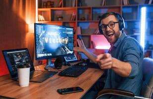 Uplifting and energized, man, is playing the shooter game on his computer. Neon lighting photo