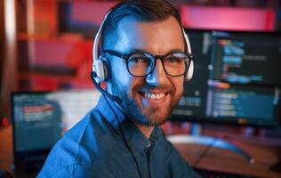 Positive, professional programmer is working indoors and smiling. Neon lighting photo