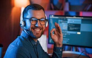 Sitting and smiling. Professional programmer ,is working indoors. Neon lighting photo