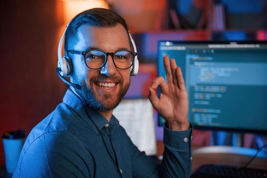 Sitting and smiling. Professional programmer is working i..ndoors. Neon lighting photo