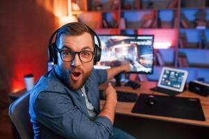 Uplifting and energized man is playing the shooter, game on his computer. Neon lighting photo