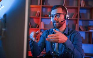 Having online meeting.. Man, is sitting, by a computer indoors at home. Neon lighting photo
