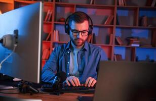 In glasses.. Man is sitting by a computer indoors at home. Neon lighting photo