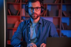 In glasses. Man is sitting ,by a computer indoors at home. Neon lighting photo