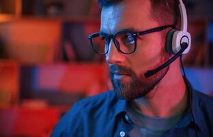 Portrait of man that, is sitting, by a computer indoors at home. Neon lighting photo