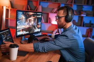 Concentrated,man, is playing the shooter game on his computer. Neon lighting photo