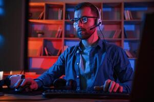 Front view. .Man is sitting by a computer indoors at home. Neon lighting photo