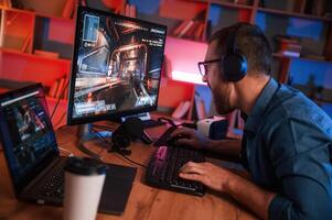 Concentrated ,man is playing the shooter game on his computer. Neon lighting photo