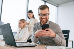 Smiling and holding, smartphone. Successful team are working together in the office. Conception of business photo
