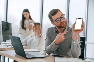 Man is ,showing information on smartphone. Successful team are working together in the office. Conception of business photo