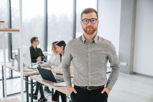 Man in glasses and formal clothes is standing. Successful team are working together in the office. Conception of business photo