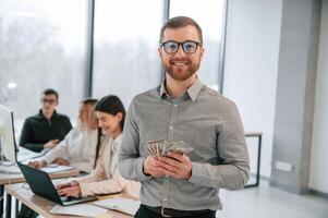 Man is with money in hands. Successful team are working together in the office. Conception of business photo