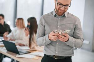 Man is holding money in, hands. Successful team are working together in the office. Conception of business photo