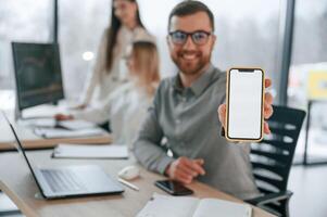 Smiling and holding smartphone. Successful team are working together in the office. Conception of business photo