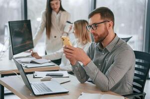 Man mis sitting and using smartphone. Successful team are working together in the office. Conception of business photo