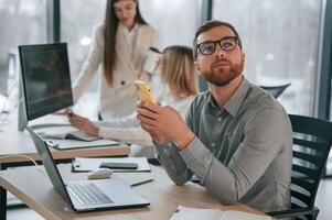 Man is sitting and using smartphone. Successful team are working together in the office. Conception of business photo