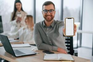 Man is showing information on smartphone. Successful team are working together in the office. Conception of business photo