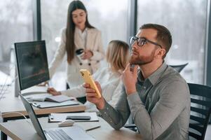 Man ,is sitting and using smartphone. Successful team are working together in the office. Conception of business photo
