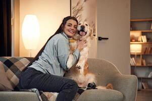 Sitting ,,on the sofa. Woman is with golden retriever dog at home photo