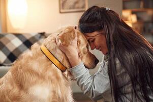 Side, view. Having, fun, embracing. Woman is with golden retriever dog at home photo