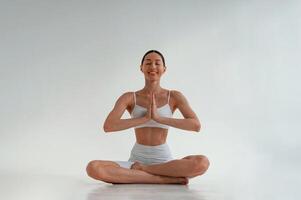 Sitting in a lotus pose. Young caucasian woman with slim body shape is indoors in the studio photo