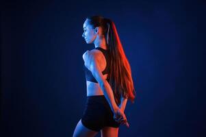 Rea,r view. Beautiful muscular woman is indoors in the studio with neon lighting photo