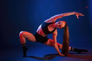 Squats, with stretching. Beautiful muscular woman is indoors in the studio with neon lighting photo