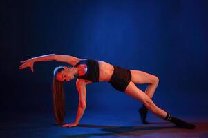 Exercise, by standing on a leg and hand. Beautiful muscular woman is indoors in the studio with neon lighting photo