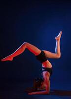 Doing ,hand stand. Beautiful muscular woman is indoors in the studio with neon lighting photo