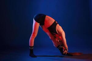 Bends to the leg, stretching. Beautiful muscular woman is indoors in the studio with neon lighting photo