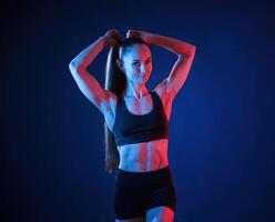 Fixes her hair. Beautiful ,muscular woman is indoors in the studio with neon lighting photo