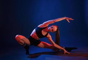 Squats with stretching. Beautiful muscular woman is indoors in the studio with neon lighting photo