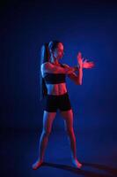 Preparing, for sportive exercises. Warm up exercises. Beautiful muscular woman is indoors in the studio with neon lighting photo